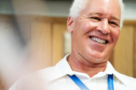Portrait of Dr. Robert Bryant smiling and in a white button up shirt with a blue lanyard